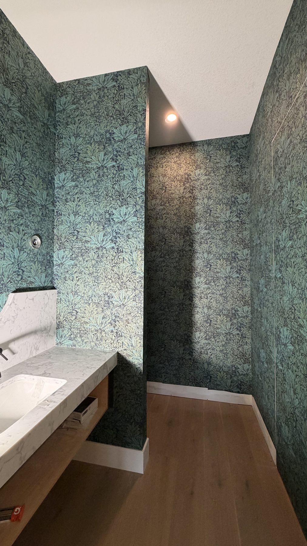 Finished bathroom with textured teal wallpaper and glass shower