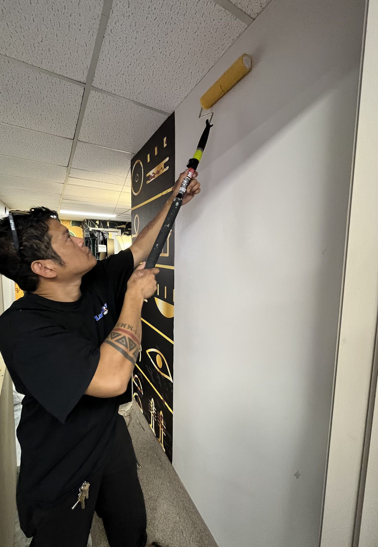 Installer applying adhesive beside black and gold wallpaper
