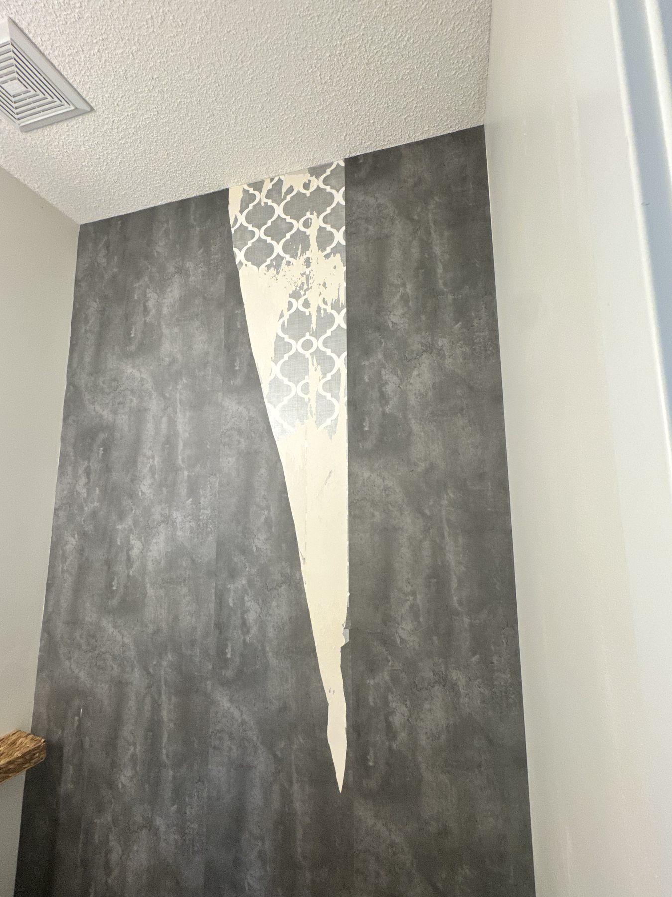 Damaged wallpaper panel with a torn section exposing the wall underneath